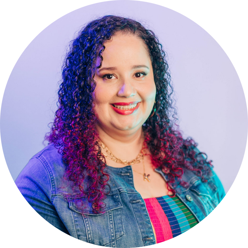 Kristine Gonzalez wearing a denim jacket, smiles at the camera against a light purple background