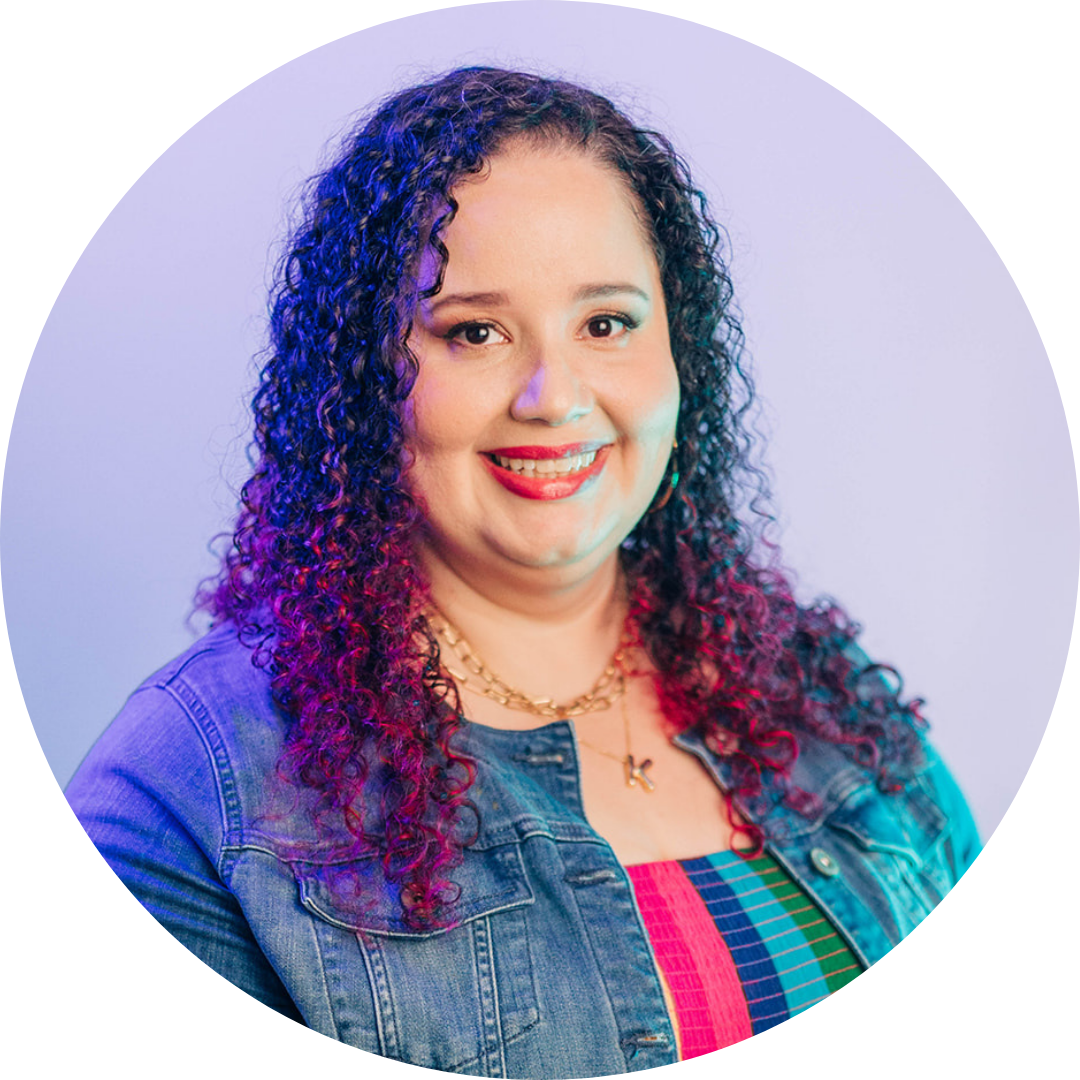 Kristine Gonzalez wearing a denim jacket, smiles at the camera against a light purple background