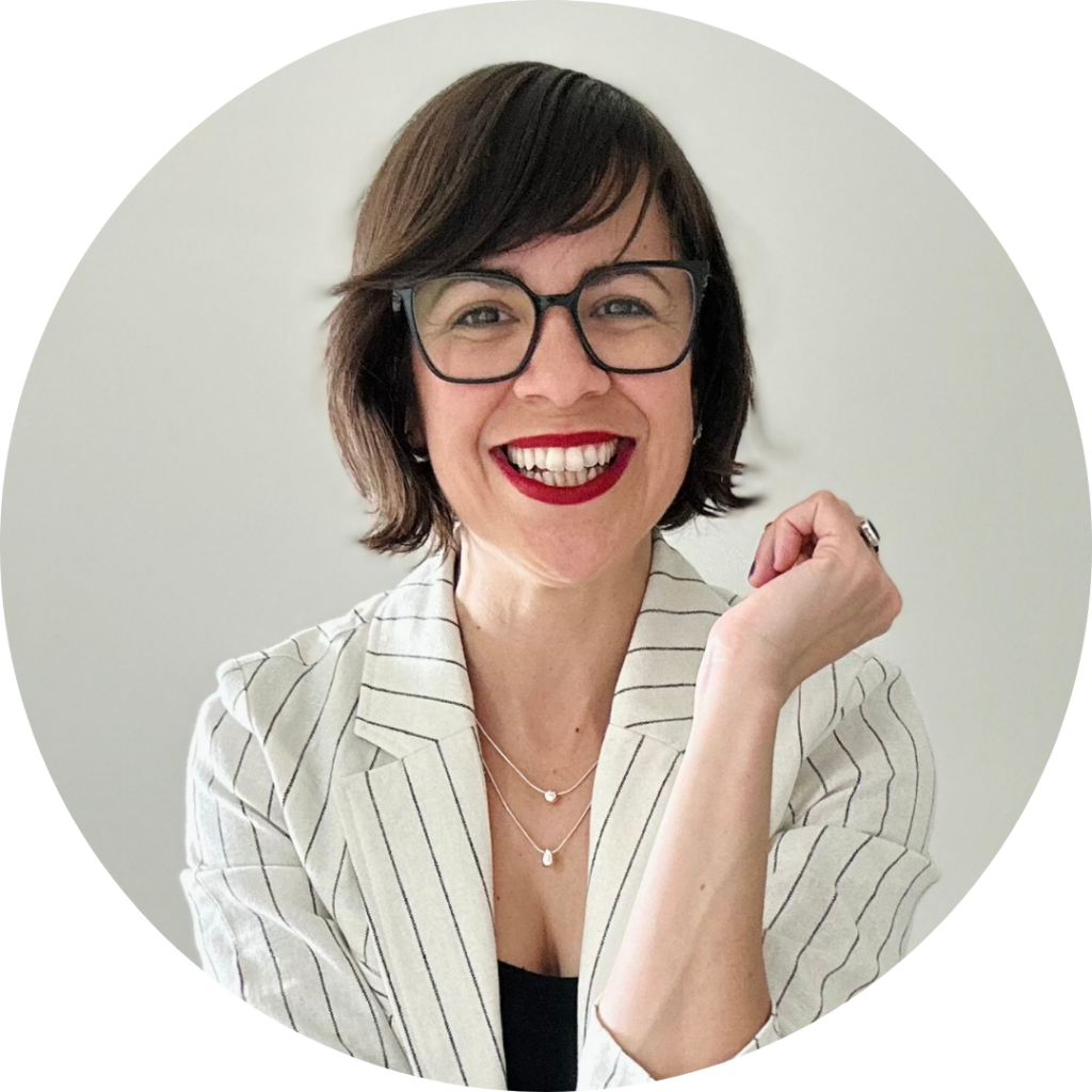 Mayra Ortiz-Nieves in a white pinstriped blazer and red lipstick, smiles at the camera, one arm in the air