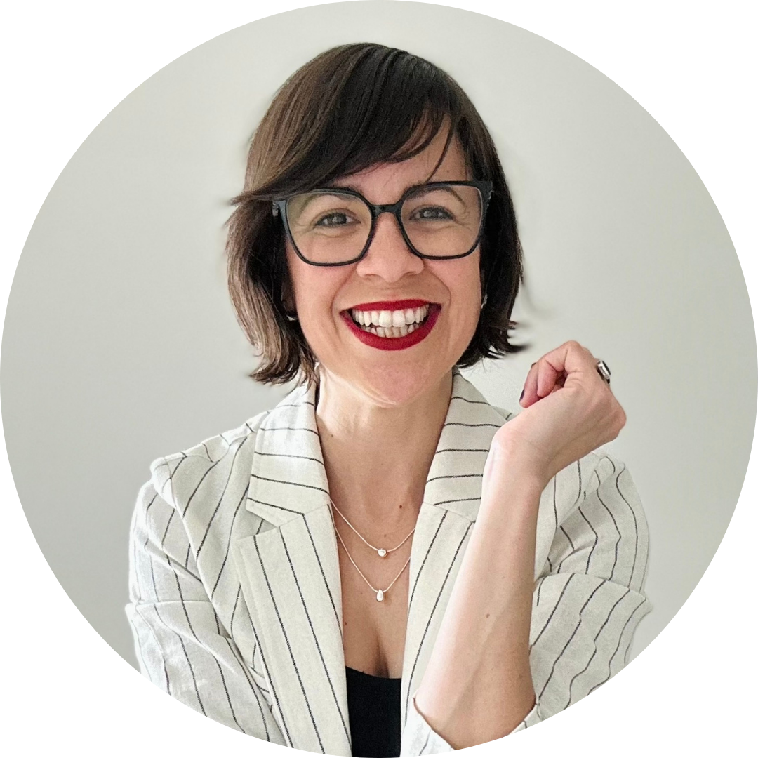 Mayra Ortiz-Nieves in a white pinstriped blazer and red lipstick, smiles at the camera, one arm in the air