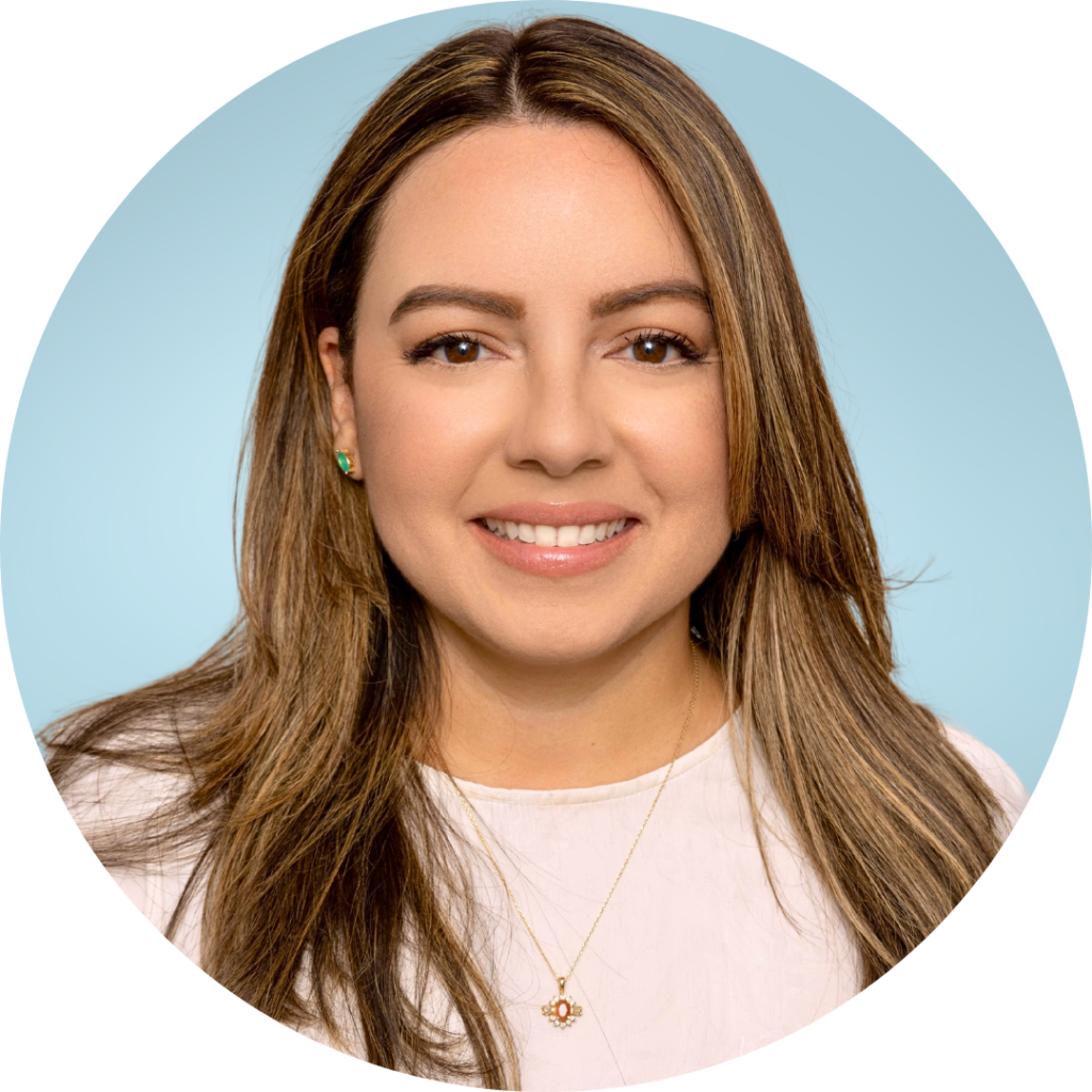 Nina Rodriguez wearing a light pink top against a blue background smiles at the camera