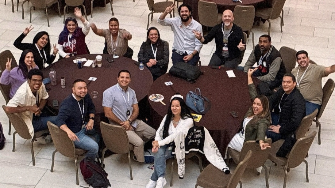 Overhead view of 15 Latines around 2 large round tables posing excitedly for the camera