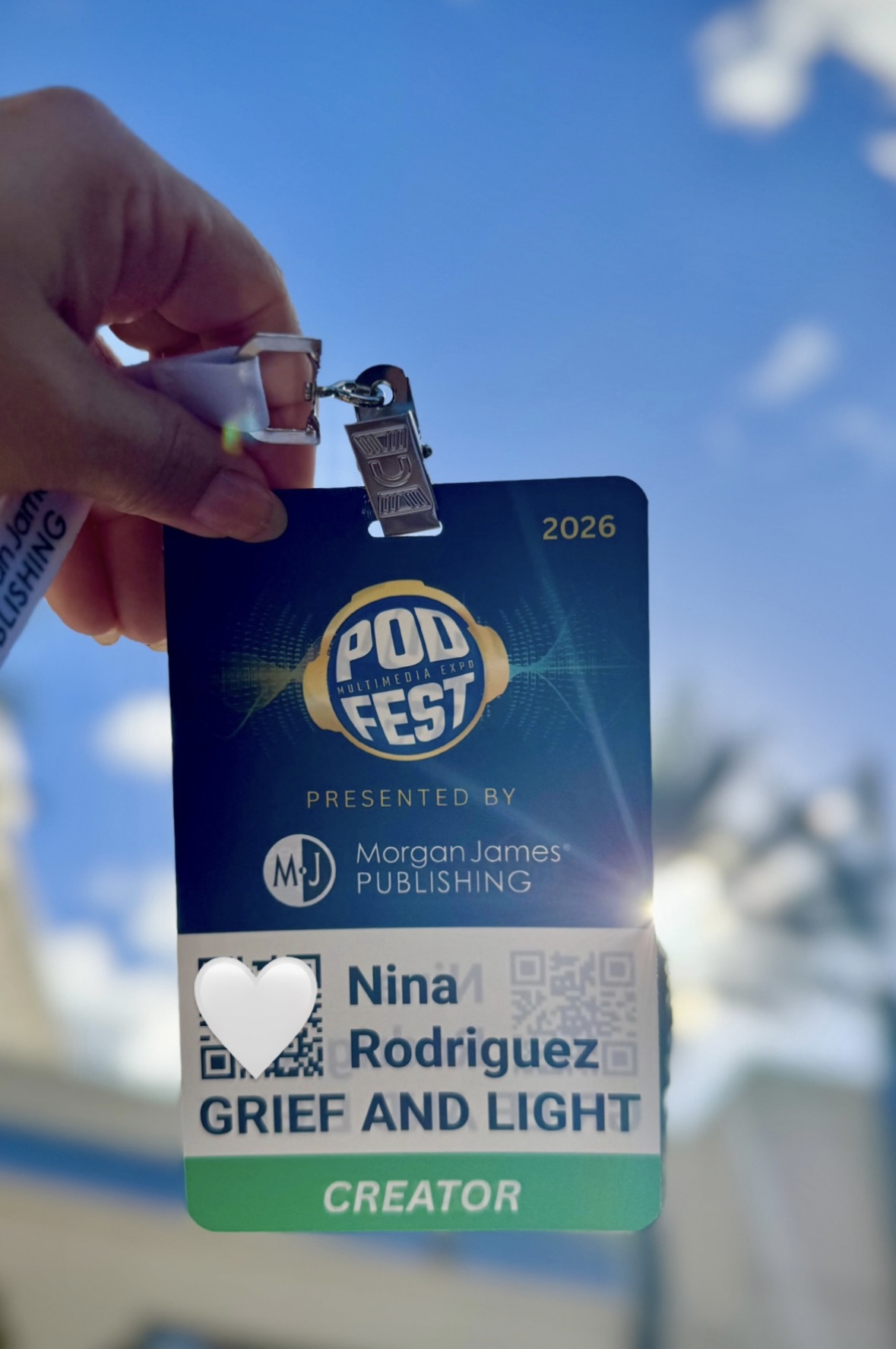 A Podfest name badge held up to the sun, reads: Nina Rodriguez GRIEF AND LIGHT, Creator