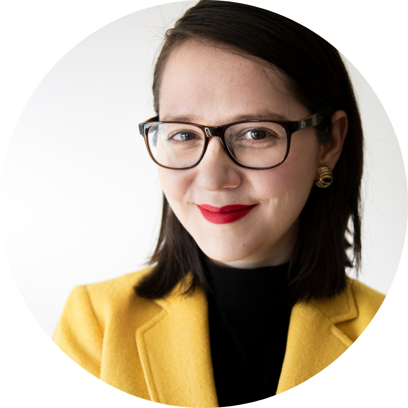 Dr. Analía Gómez Vidal smiling at the camera wearing glasses, a dark shirt, and yellow blazer