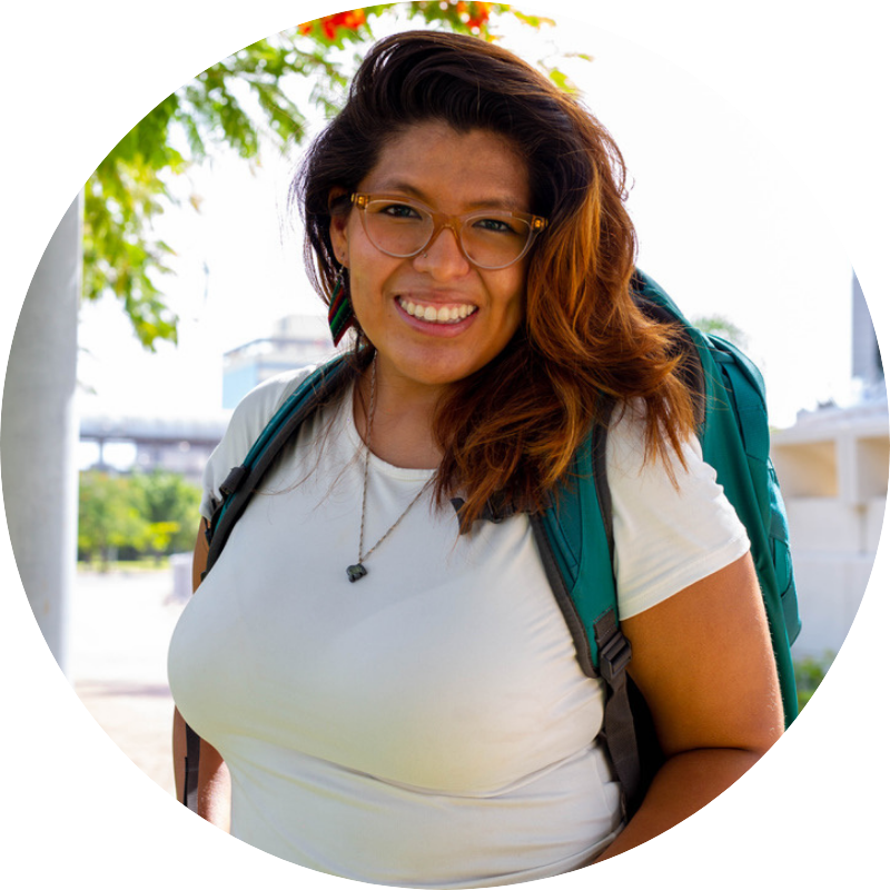 Bianca Alba in a white t-shirt and necklace wearing a turquoise backpack