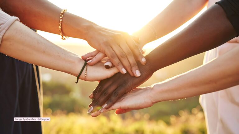 Diverse hands stacked together in unity, the sun casting a golden light behind them