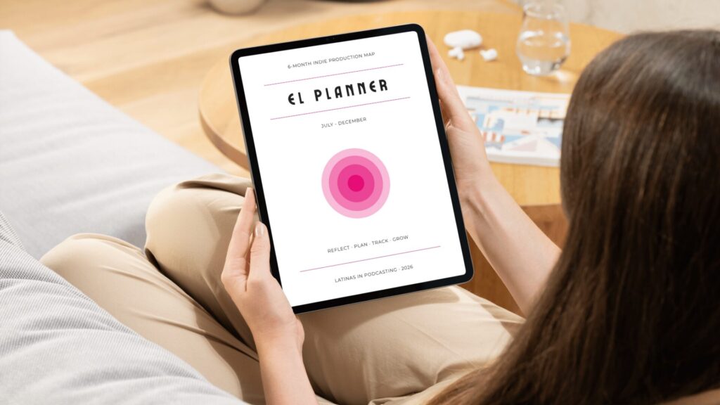 A dark haired woman sits on a couch holding a tablet which displays the cover of El Planner: A 6-month indie production map to reflect, plan, track, and grow. A large set of concentric hot pink circles, getting deeper towards the middle, dominate the center of the cover.