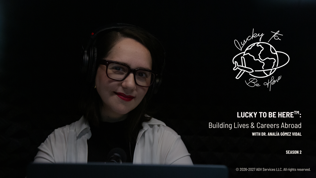 Dr. Analía Gómez Vidal smiles at the camera wearing headphones, glasses, red lipstick, and a white shirt in a dark recording booth. Season 2 cover art for Lucky To Be Here™: Building Lives & Careers Abroad, with a hand-drawn logo of a globe and an airplane. La Dra. Analía Gómez Vidal sonríe a la cámara con audífonos, lentes, labios rojos y una camisa blanca en una cabina de grabación oscura. Portada de la segunda temporada de Lucky To Be Here™: Building Lives & Careers Abroad, con un logo dibujado a mano de un globo terráqueo y un avión.